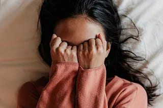 A woman lying in bed with both hands pressed over her eyes