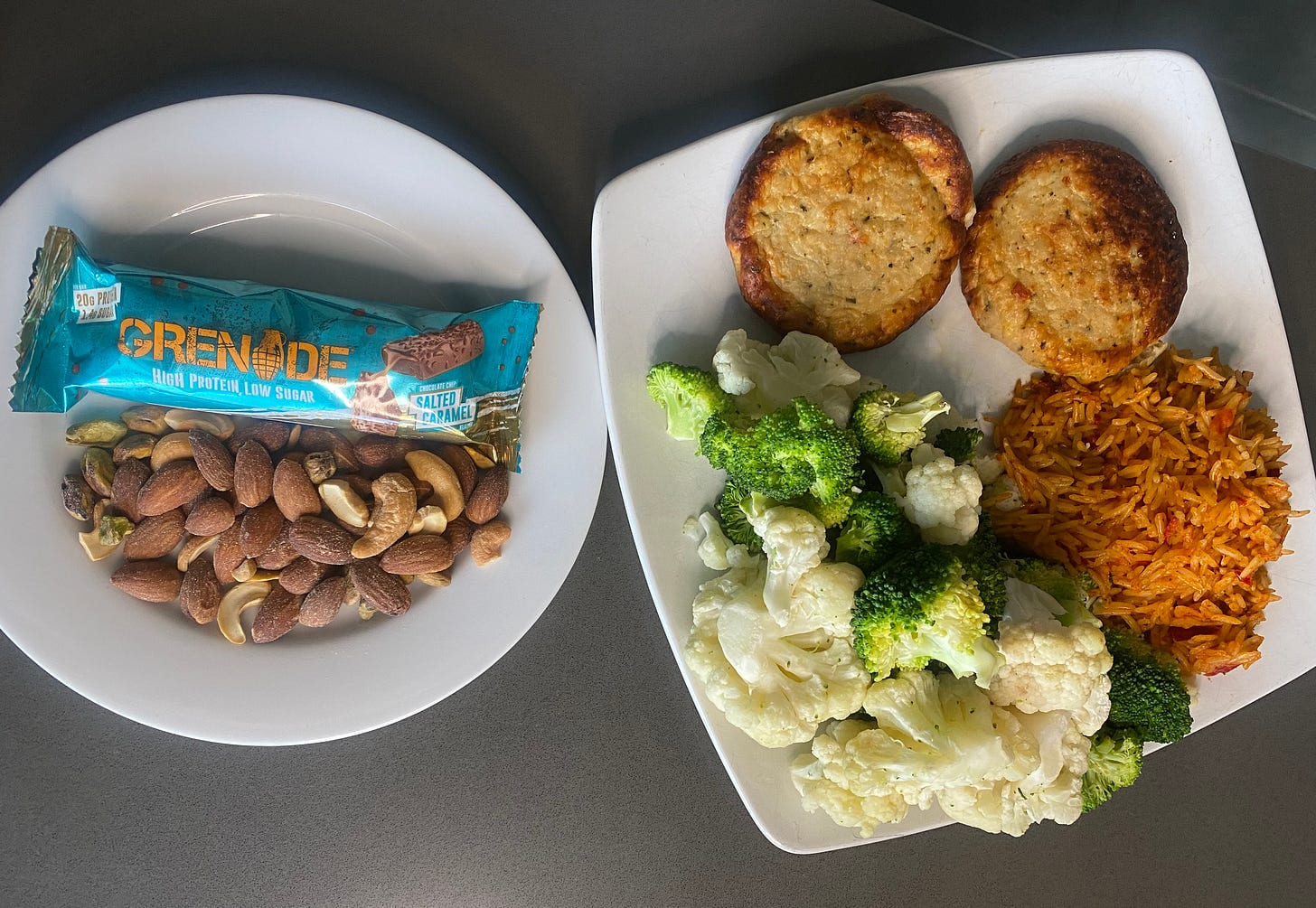 A protein bar and a bowl of mixed nuts beside a plate of roast potatoes, broccoli, cauliflower and sweet potato
