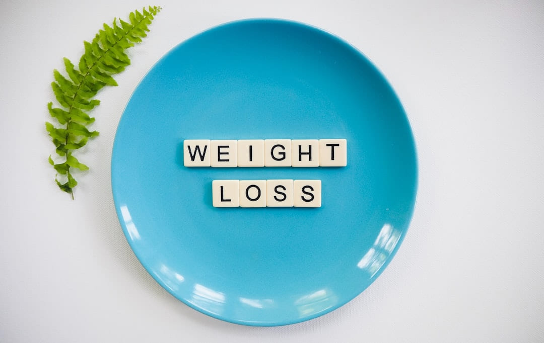 Letter tiles spelling the words weight loss on a blue plate beside a fern leaf