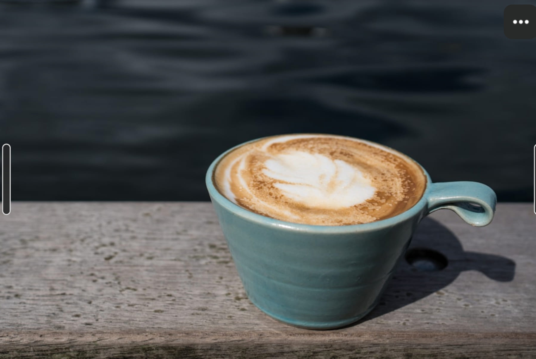 A cappuccino in a pale green cup on a stone surface