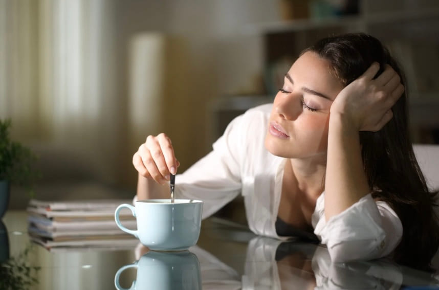 A woman resting her head on one hand as she stirs a cup of coffee at a desk