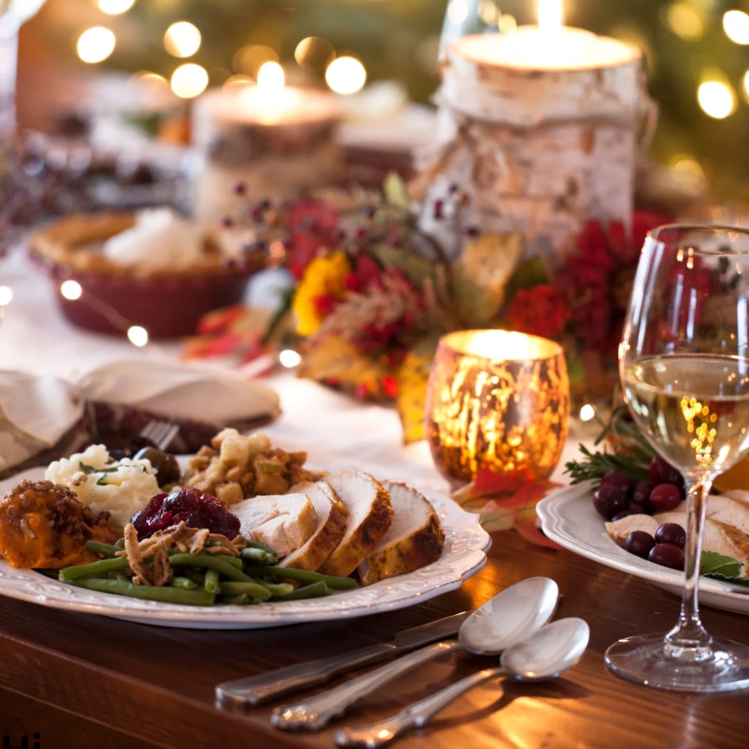 A festive dinner table set with roast turkey, vegetables, candles and wine