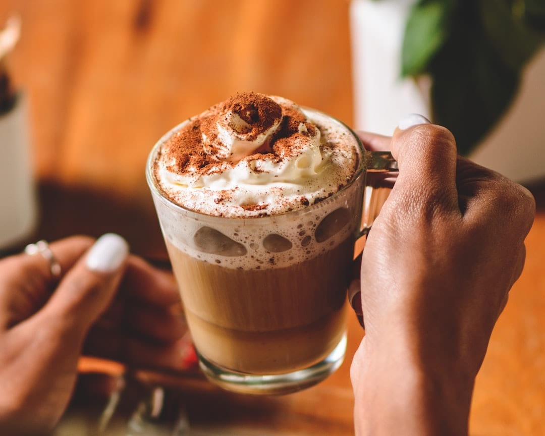Hands holding a tall glass of frothy coffee dusted with cocoa