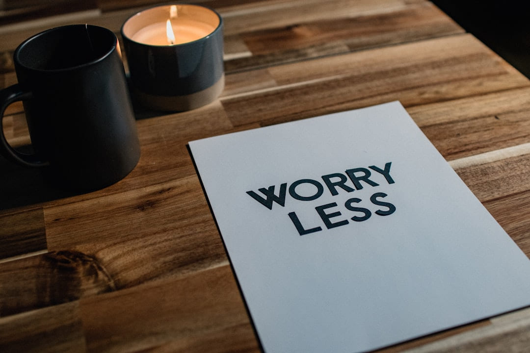 A card printed with the words worry less on a wooden table beside two mugs and a candle