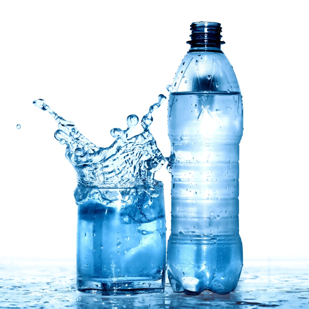 A plastic water bottle beside a glass of water mid-splash
