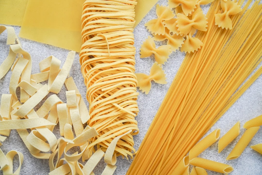 Dried tagliatelle, farfalle and spaghetti arranged on a pale surface