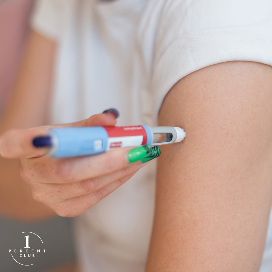 A hand holding an injector pen against the back of an upper arm