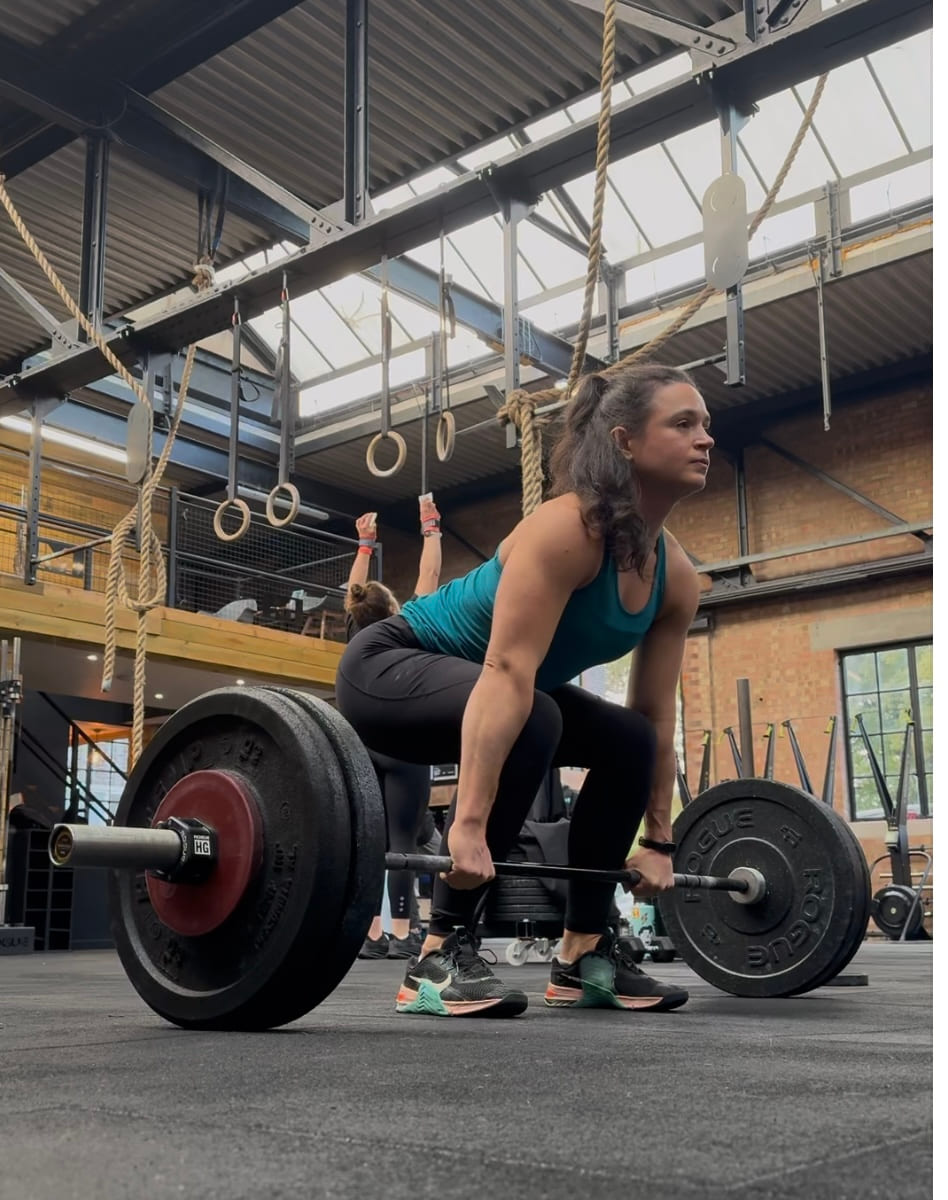 A woman lifting a loaded barbell from the floor in a warehouse gym