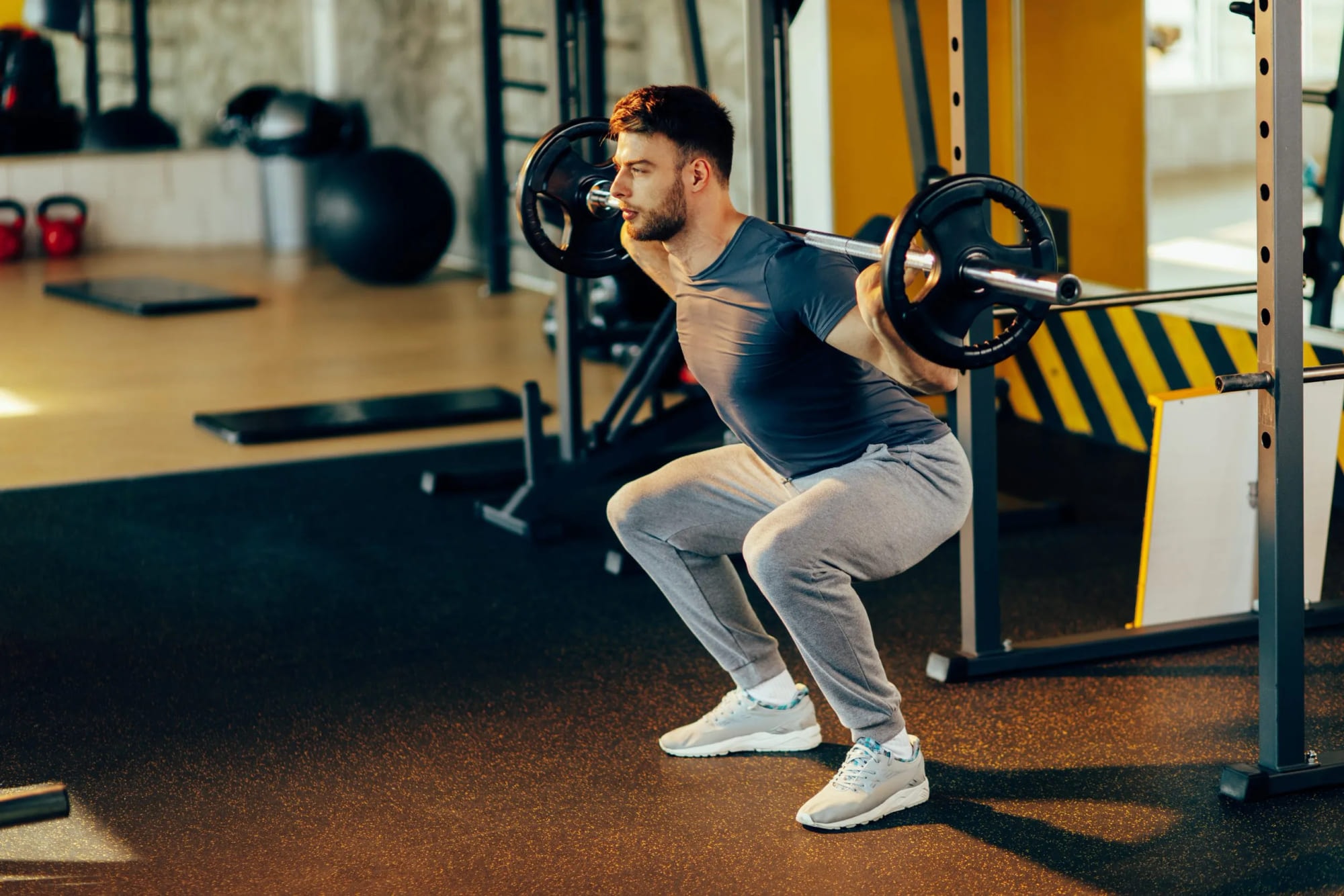 A man squatting with a barbell across his shoulders in a gym