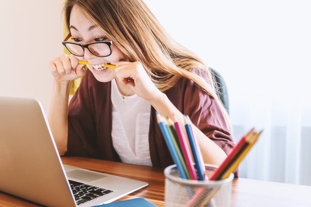 A woman at a laptop biting the end of a pencil