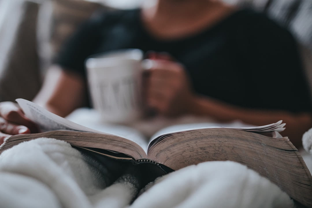 A person reading in bed holding a mug of tea