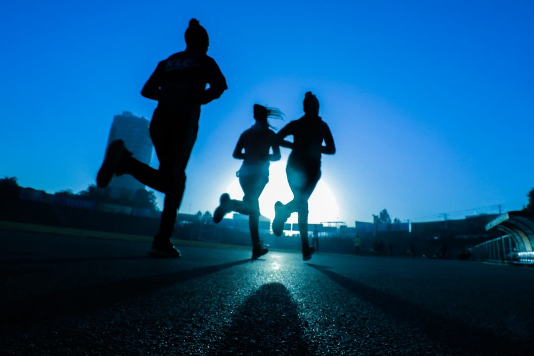 Silhouettes of three runners against a bright dawn sky