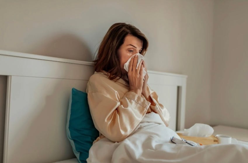 A woman sitting up in bed blowing her nose