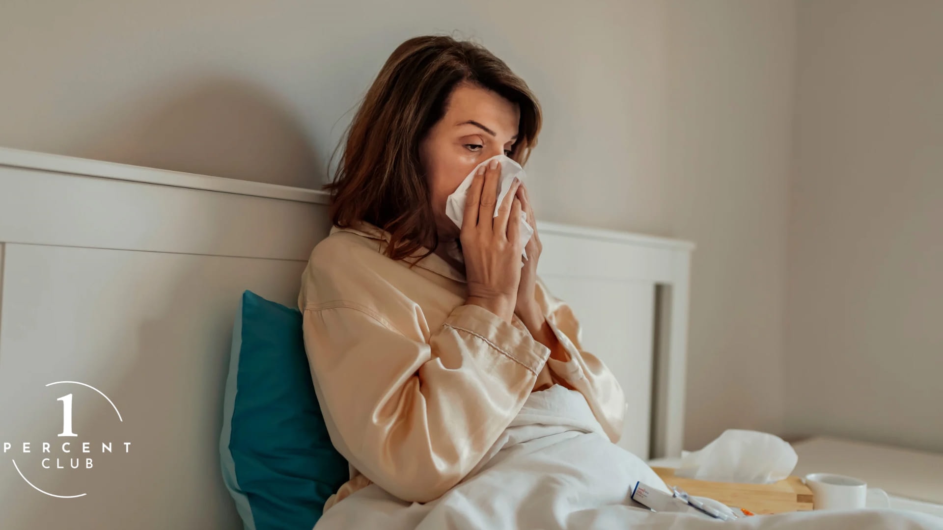 A woman propped up in bed with a cold, blowing her nose