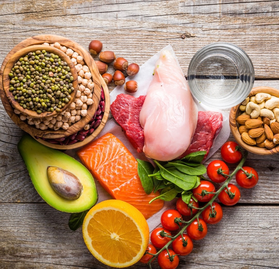 Salmon, chicken, avocado, pulses, tomatoes and citrus arranged on a wooden board