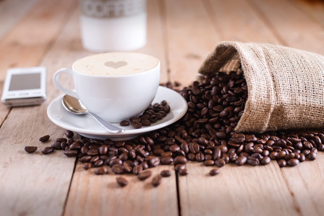 A cappuccino beside a spilled sack of coffee beans on a wooden table