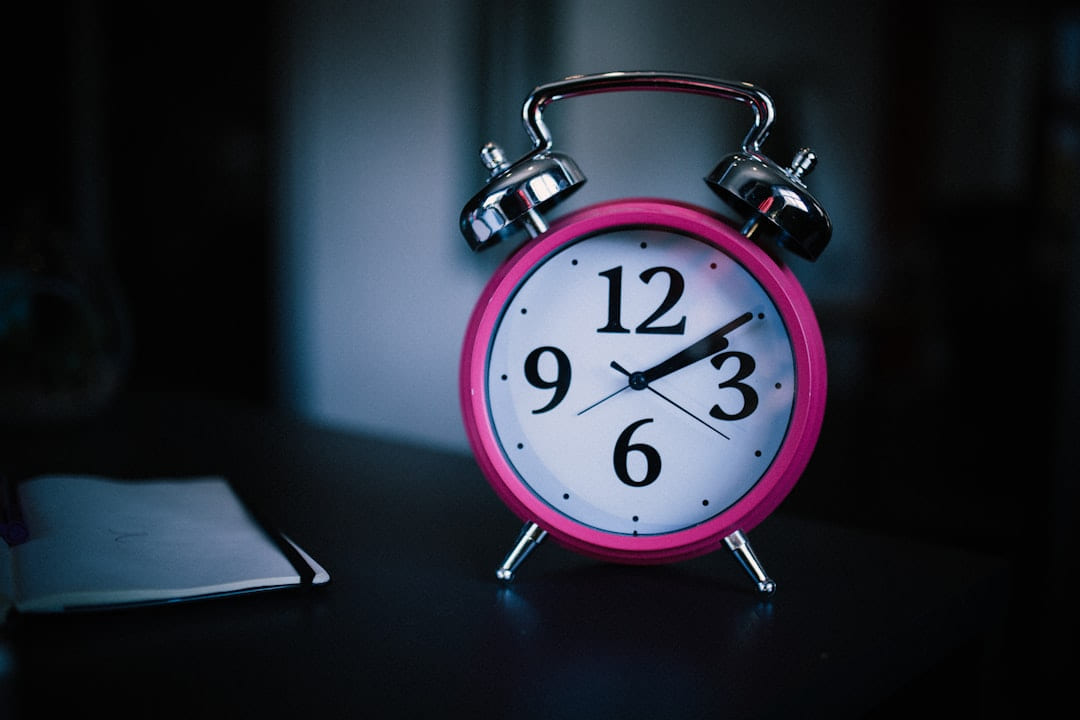 A pink alarm clock on a bedside table in a dark room