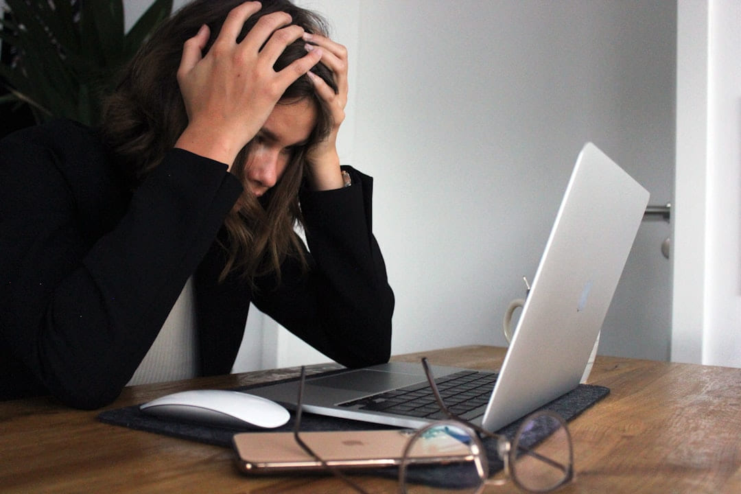 A woman at a desk with both hands in her hair, a laptop open in front of her