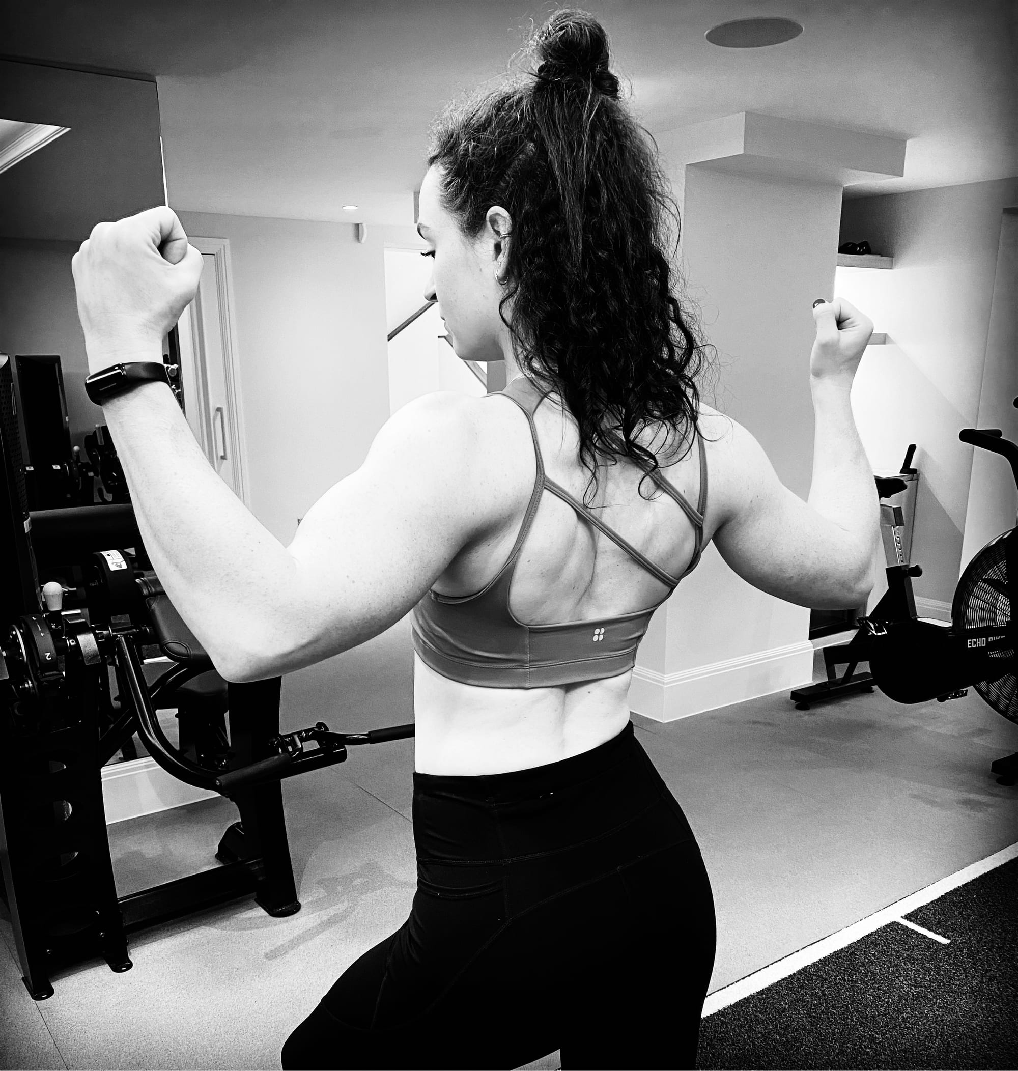 A black and white photograph of a woman pulling a cable machine in a gym