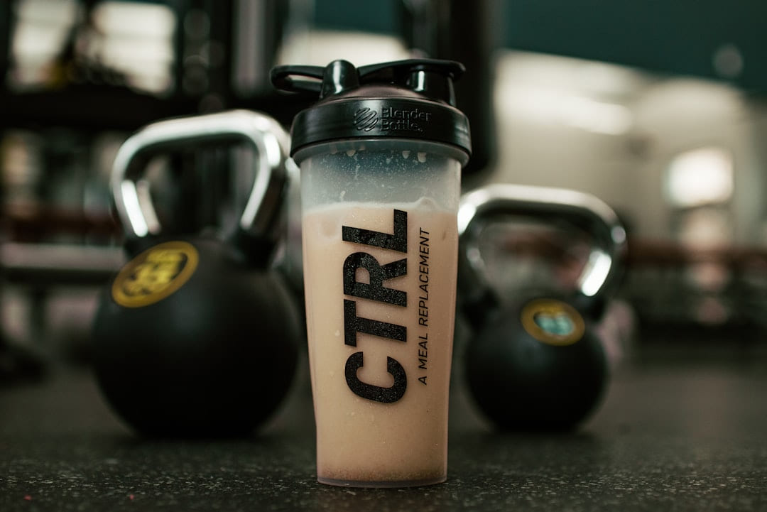 A protein shaker standing between two kettlebells on a gym floor