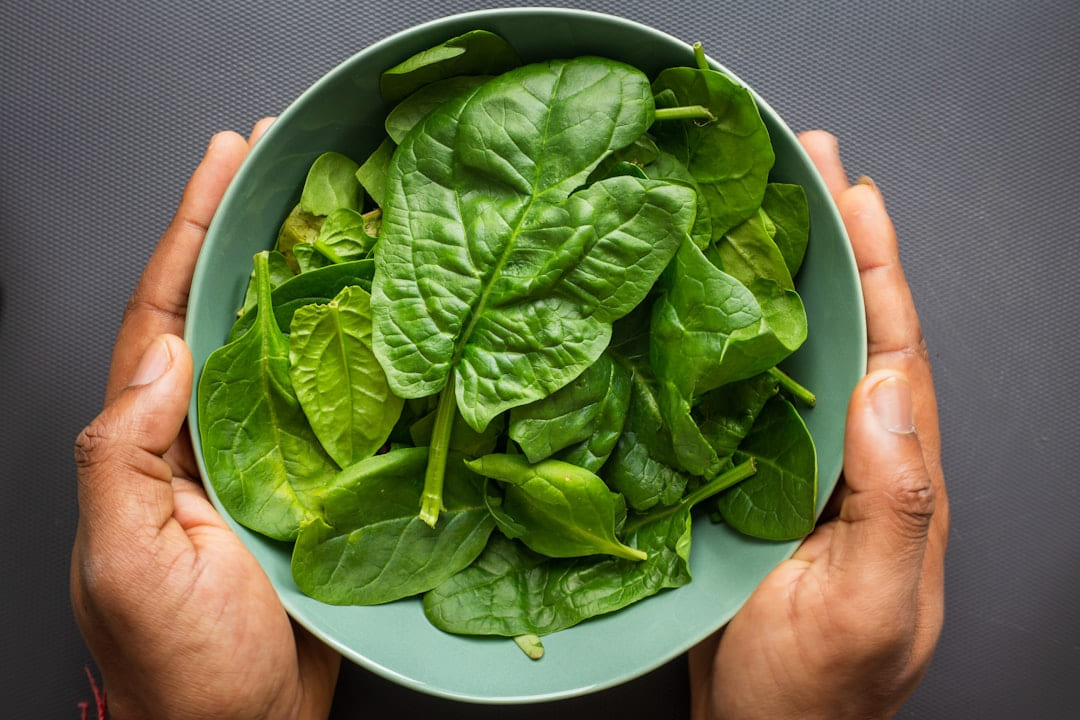 Two hands holding a bowl of fresh spinach leaves