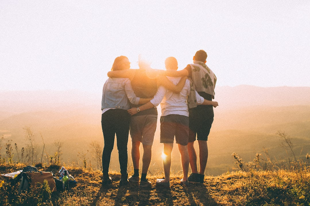 Four people standing arm in arm looking out at a sunset