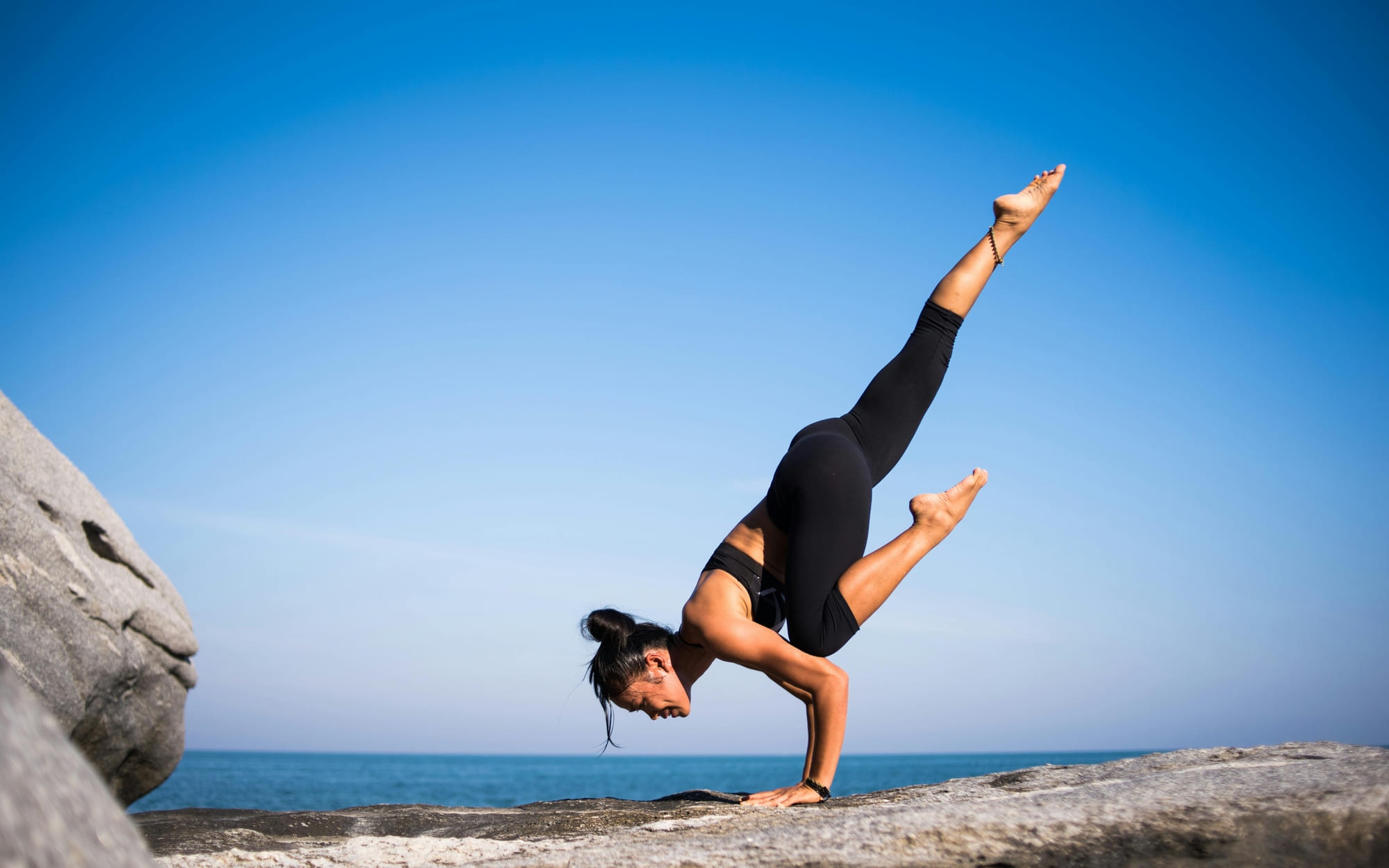 A woman holding a handstand on a rock above the sea