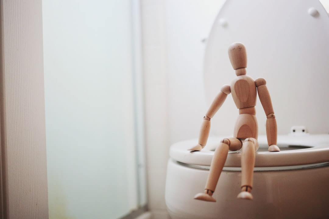 A wooden artist's mannequin sitting on a toilet