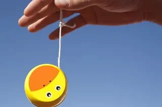 A hand holding a yellow yo-yo against a blue sky