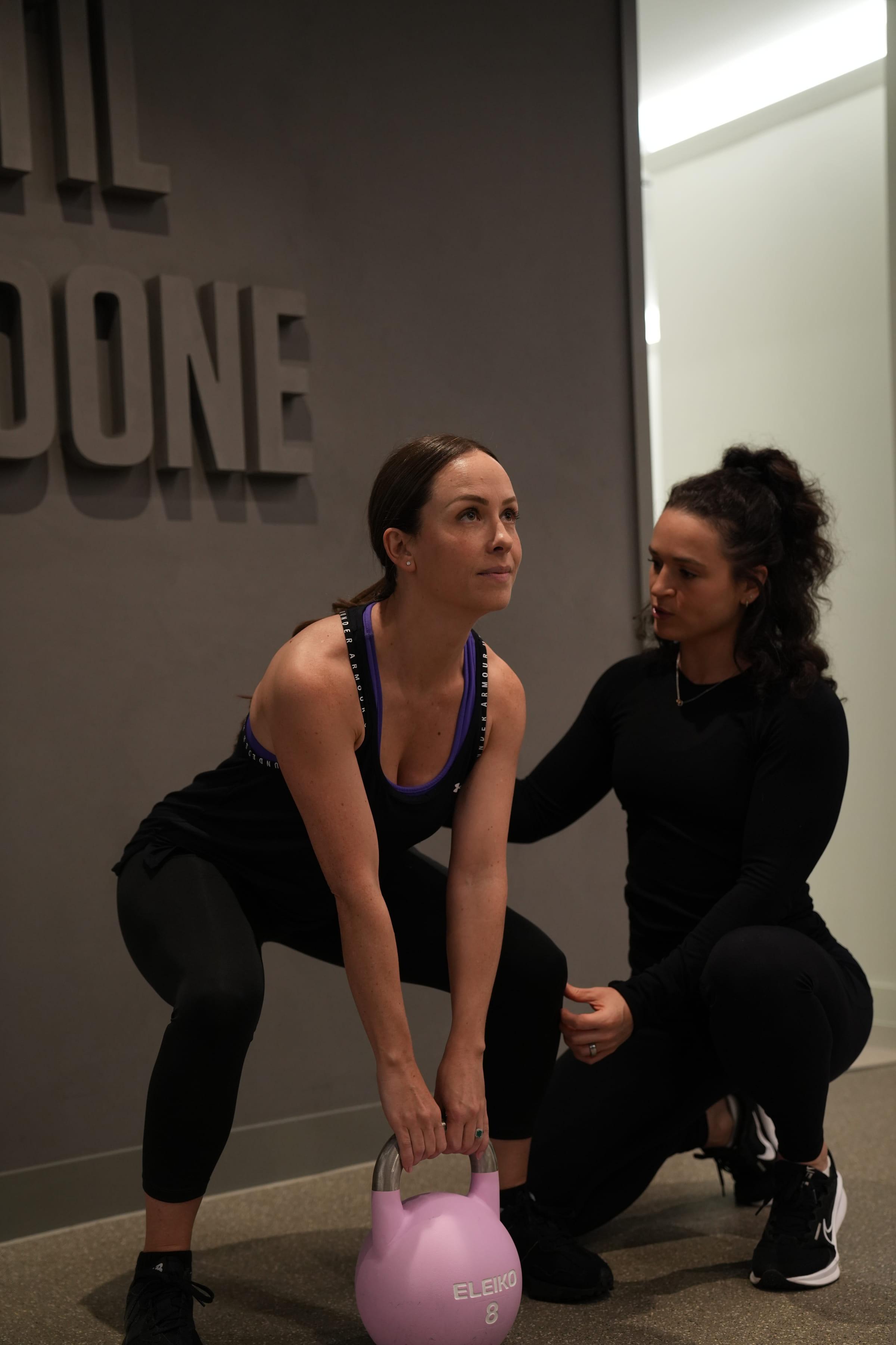 A coach kneeling beside a client mid kettlebell squat in the studio's private room