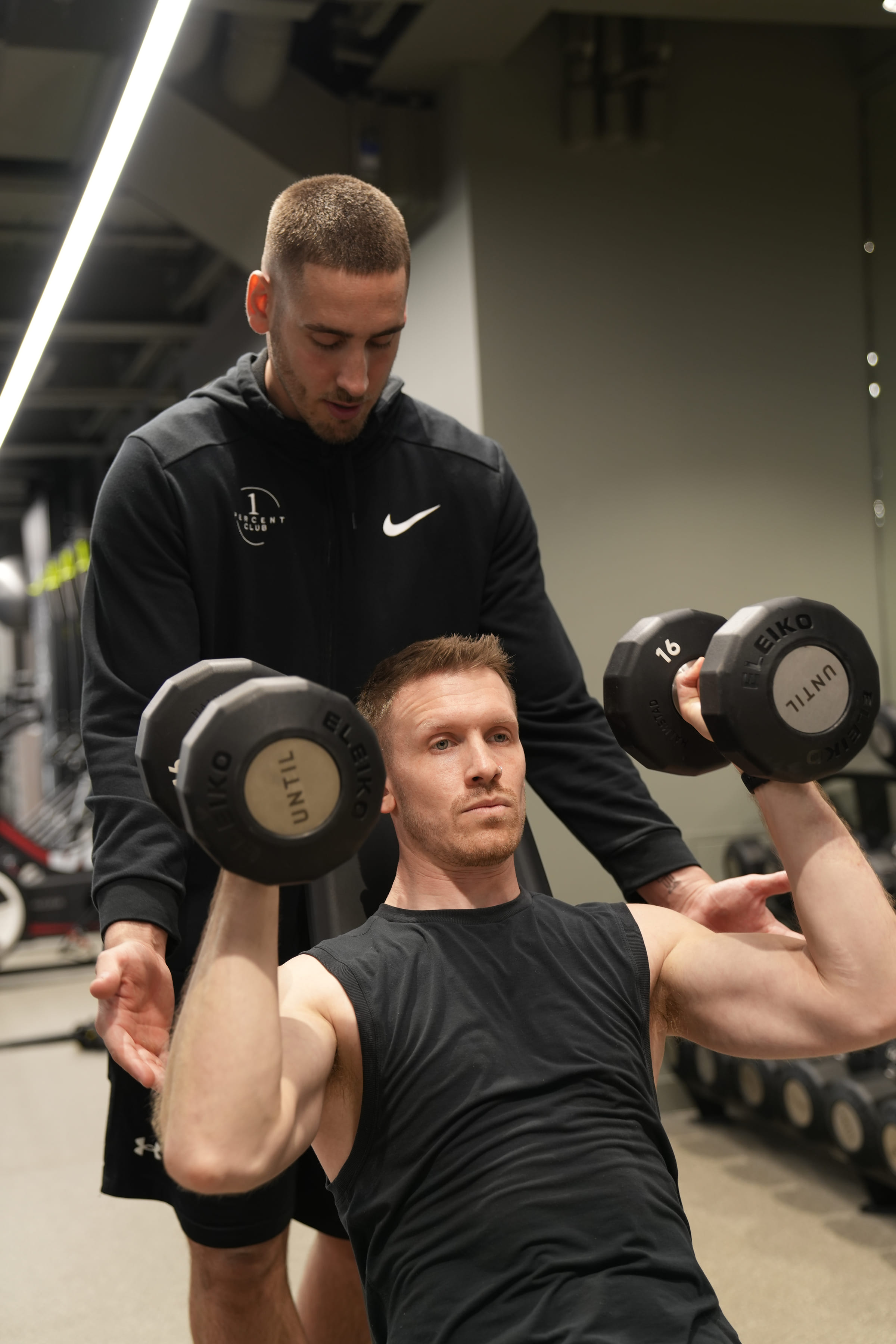 A coach spotting a client through a seated dumbbell press
