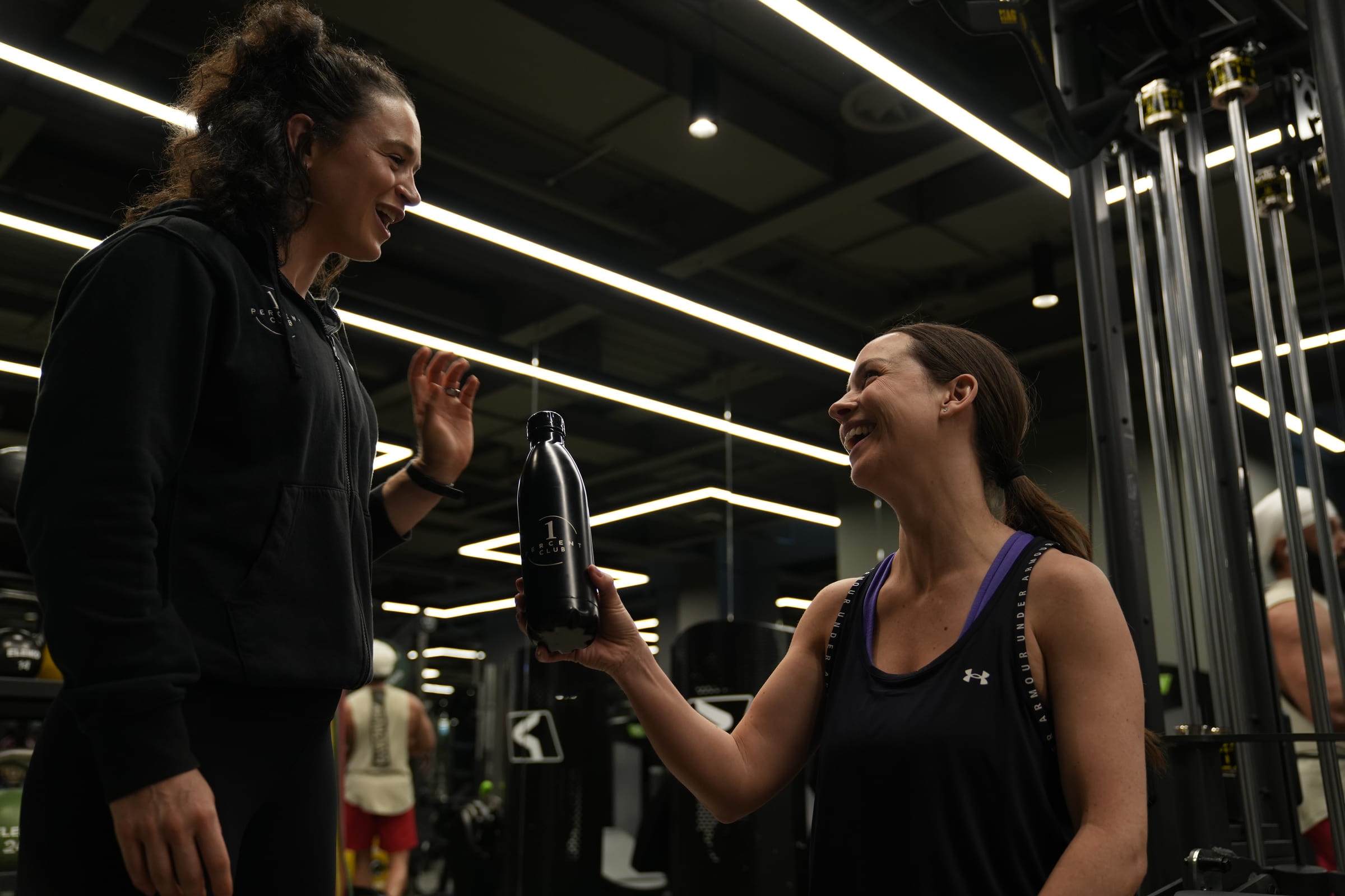 A coach and client laughing over a water break between sets