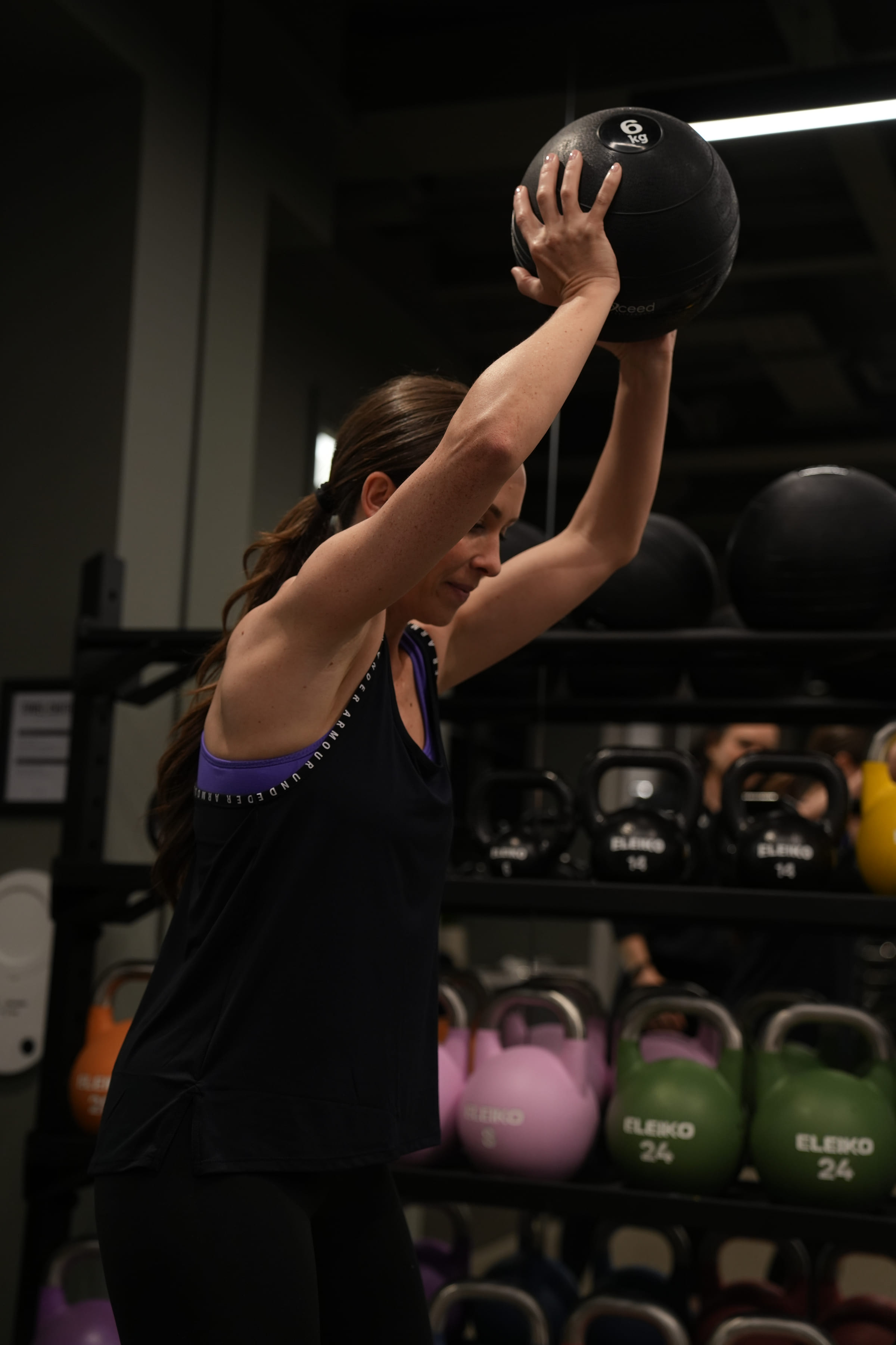 A client pressing a weighted ball overhead with a coach watching her form